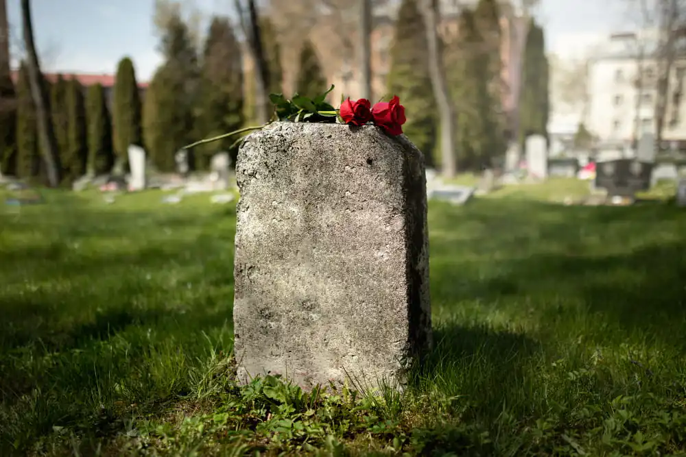 Franke Naturstein - Verwitterter Grabstein mit roten Rosen auf dem Friedhof